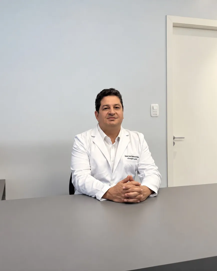 Dr. Carlos Fabiano de Oliveira, de jaleco, sentado à mesa do consultório