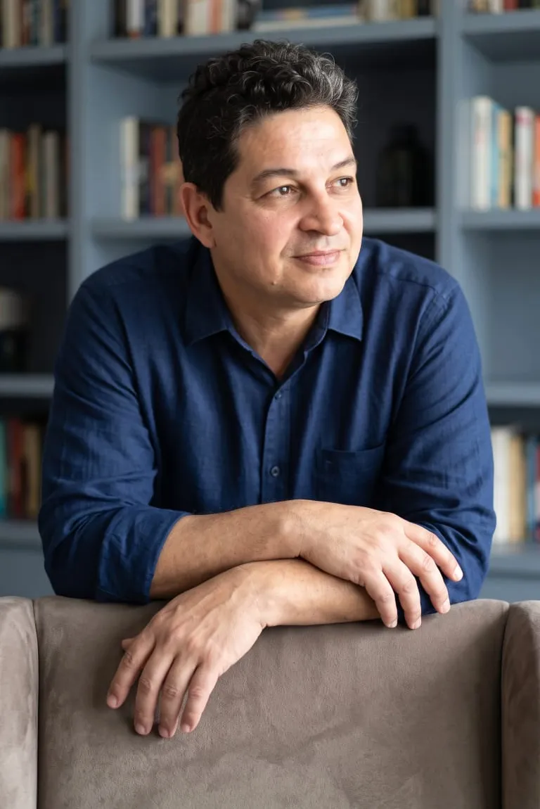 Dr. Carlos Fabiano de Oliveira, de camisa azul, apoiado no encosto de um sofá