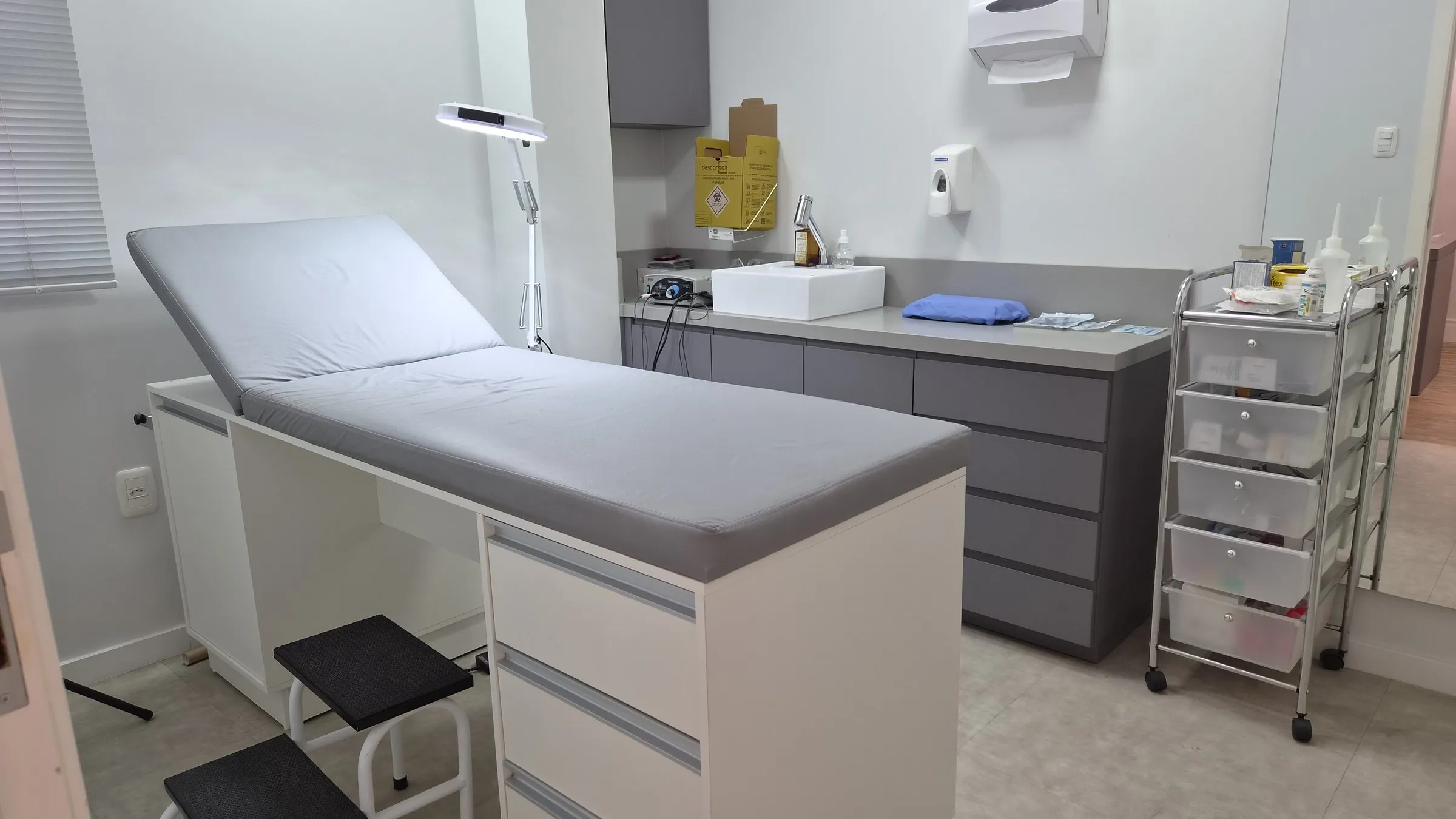 Sala de procedimentos do consultório, com maca, luminária, pia e armários